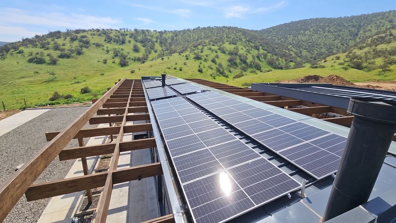 Módulos fotovoltaicos montados sobre la cubierta de una casa, con cerros verdes al fondo
