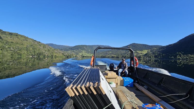 Embarcación trasladando perfiles de montaje por un lago hacia la obra
